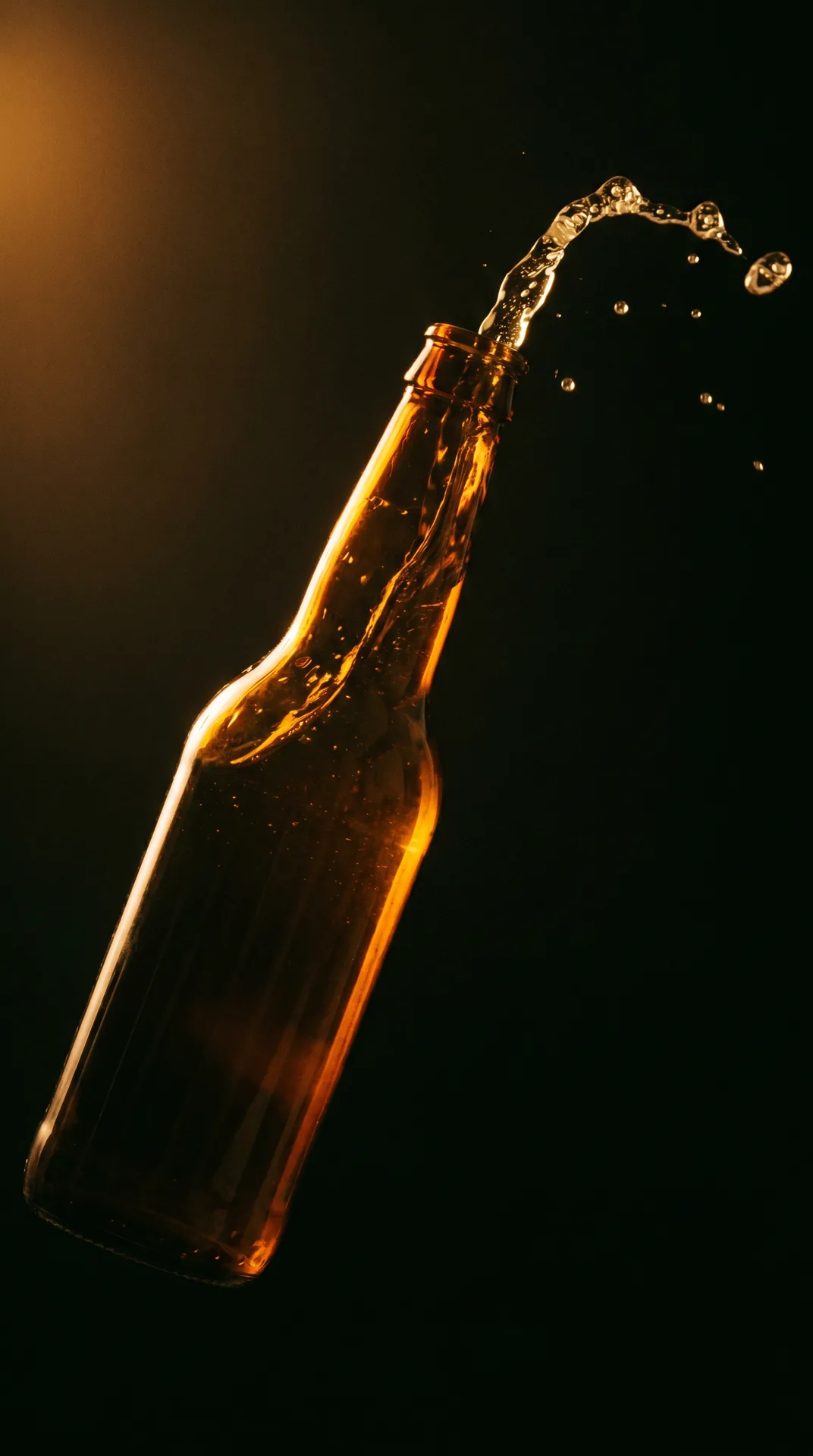 Vertical still of an amber-glass bottle mid-pour against a black backdrop.